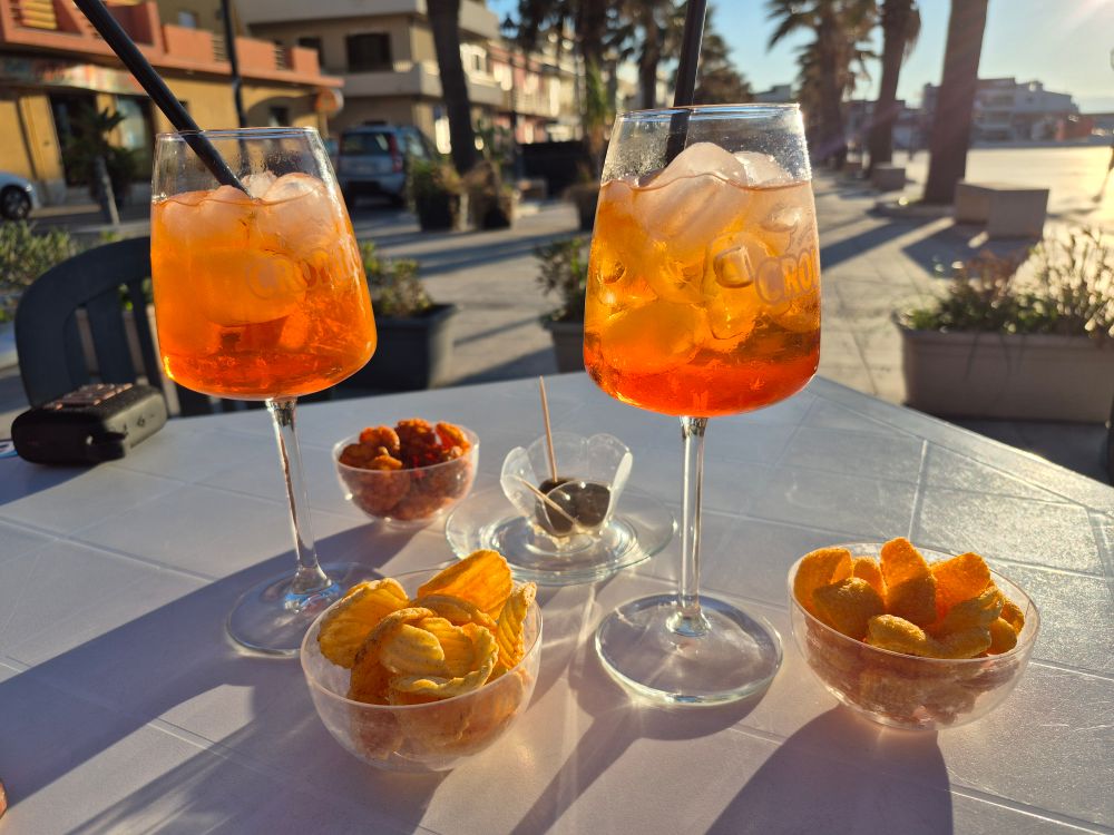 Due spritz con ciotole di stuzzichini su un tavolo all'aperto